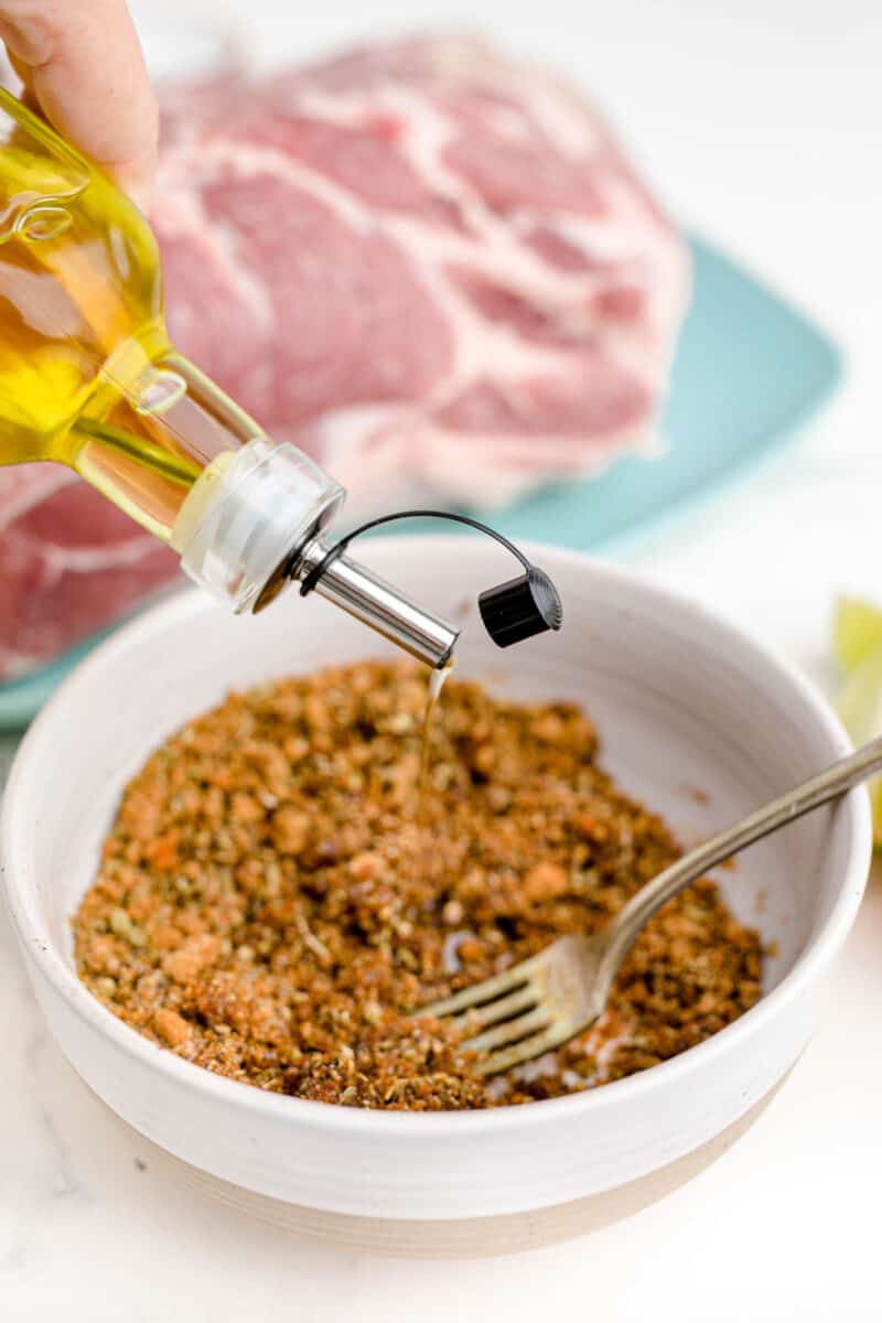 olive oil is held above a bowl of seasonings.