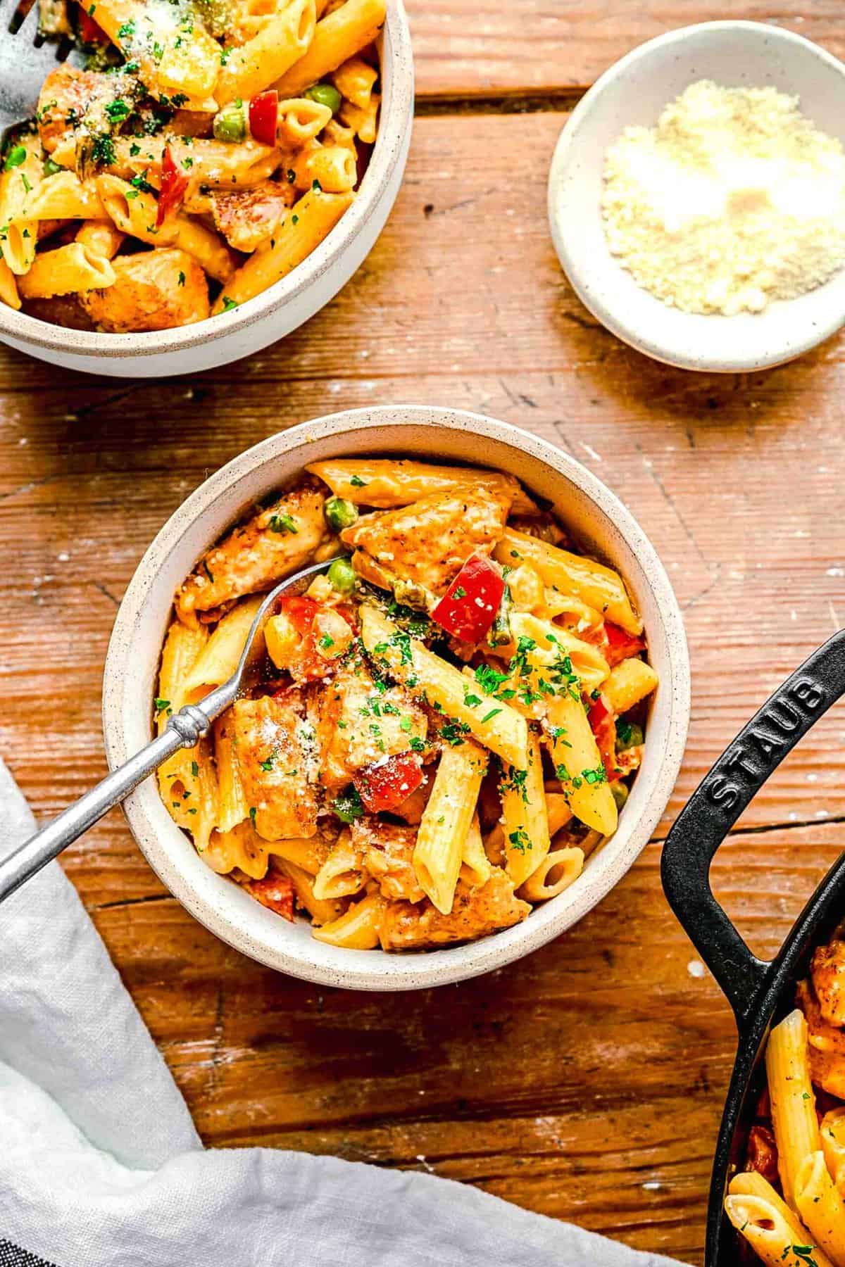 Spicy chicken chipotle pasta in bowls with a fork near a small bowl of grated parmesan cheese.