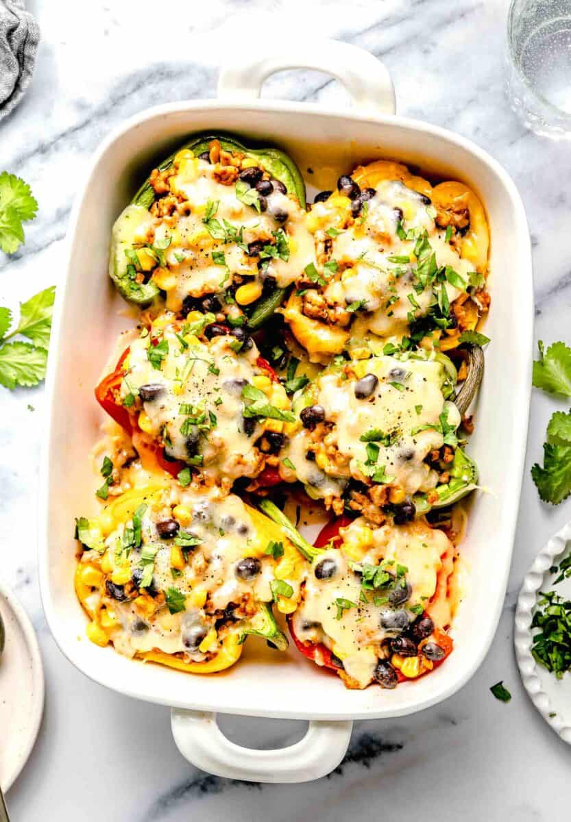 stuffed peppers with cheese and fresh herbs sprinkled on top in a white casserole dish