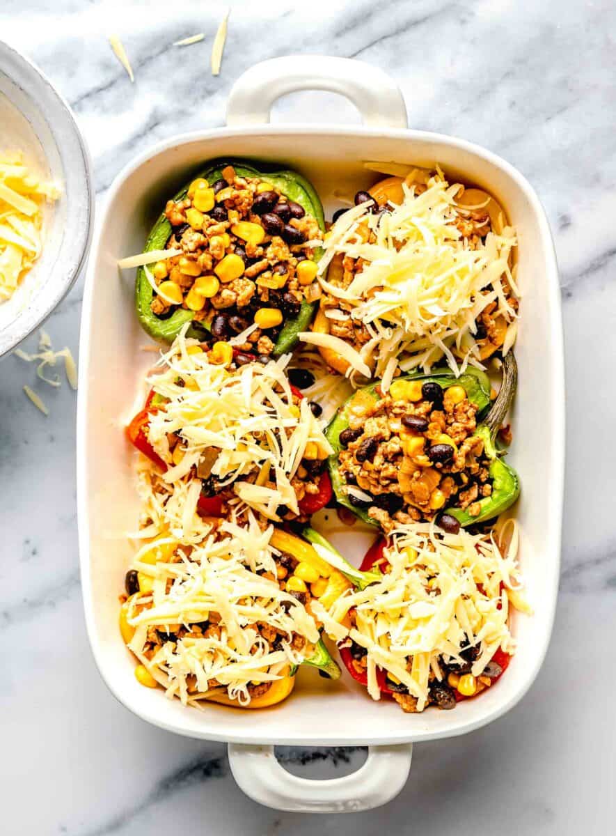 stuffed peppers in a white baking dish with unmelted cheese sprinkled on top