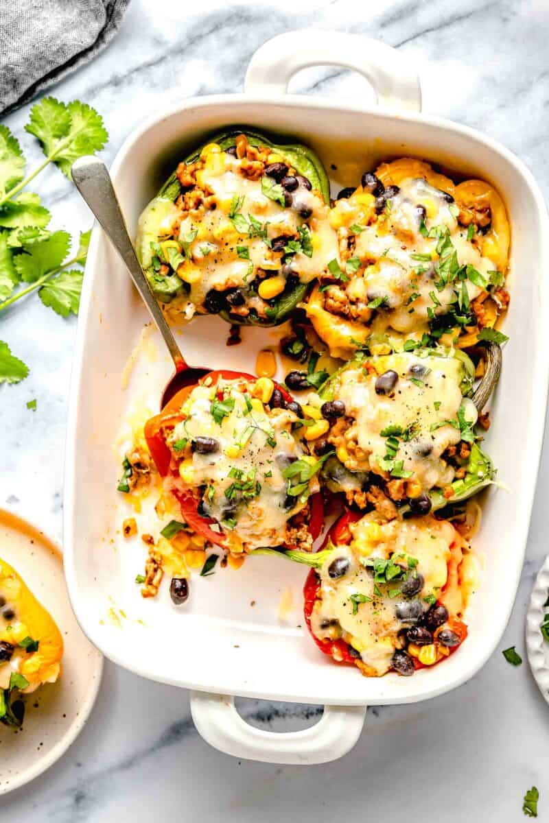 stuffed peppers in a white casserole dish with a metal spoon under the red bell pepper