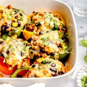 stuffed peppers in a white baking dish next to glasses of water