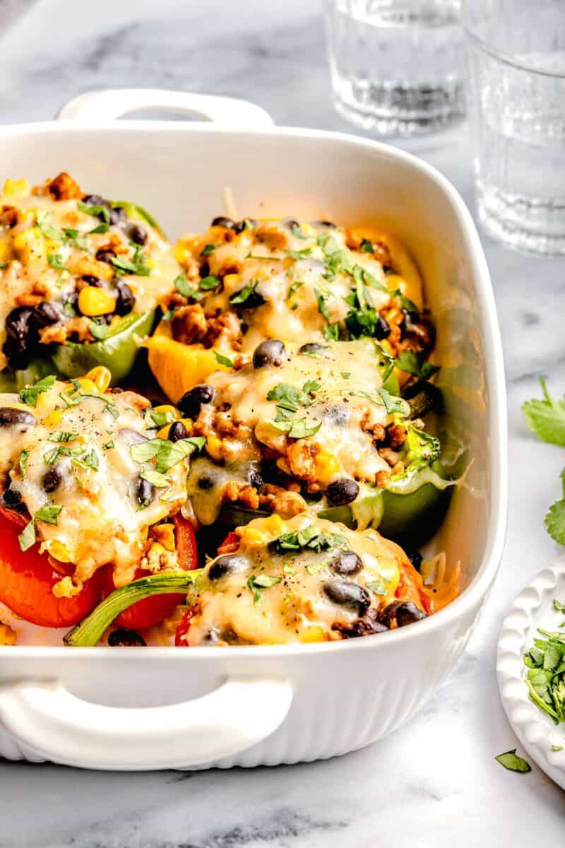 stuffed peppers in a white baking dish next to glasses of water