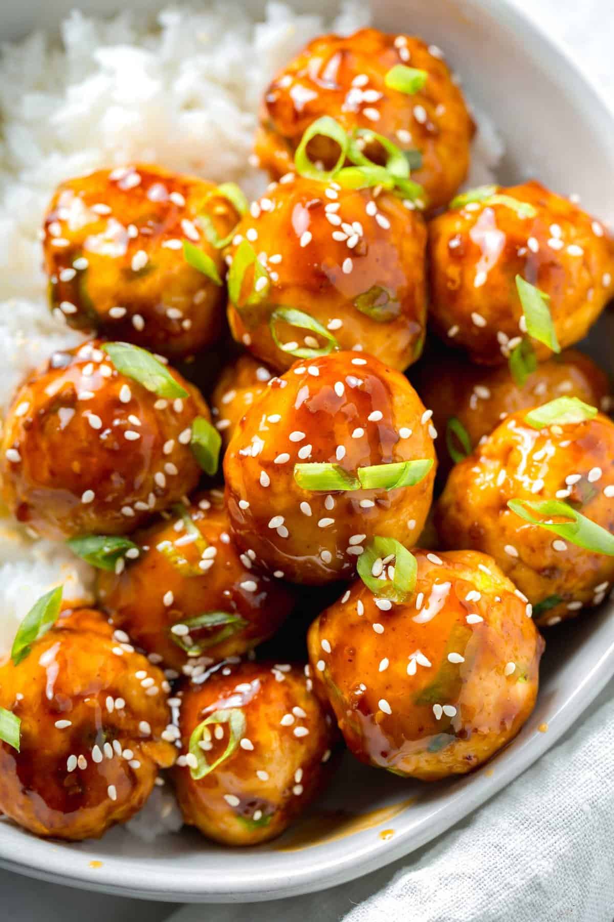 up close image of teriyaki chicken meatballs glazed in teriyaki sauce with fresh scallions and sesame seeds