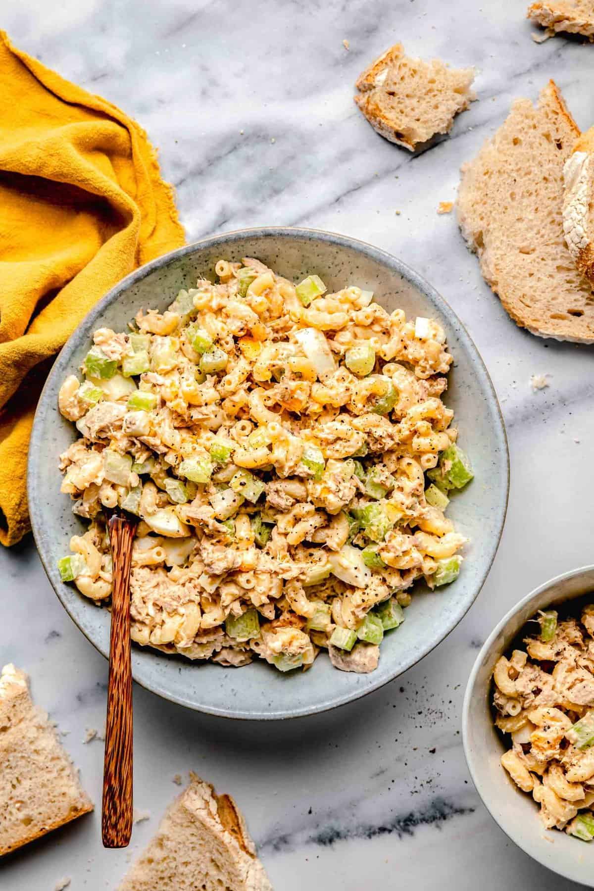 Overhead of tuna pasta salad in a bowl with a wooden spoon near bread.