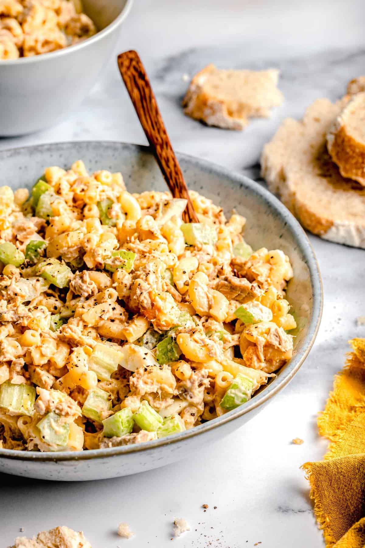 Tuna pasta salad in a bowl with a wooden spoon near bread.