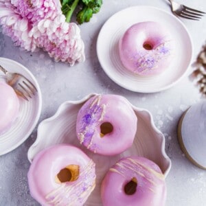 several baked and frosted donuts are placed all around various white plates