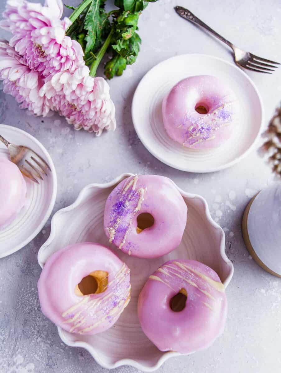 several baked and frosted donuts are placed all around various white plates