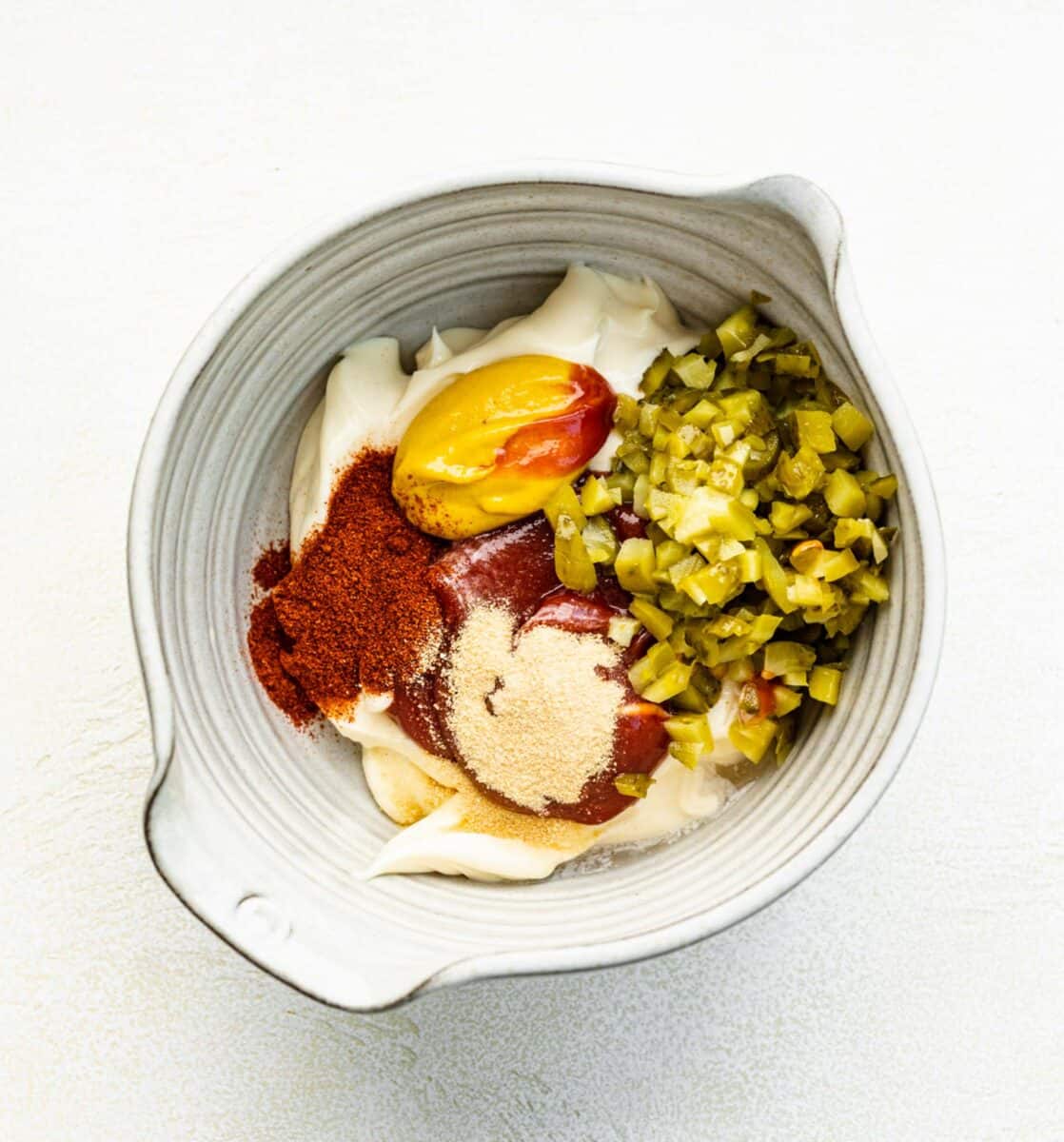 Adding ingredients for Big Mac salad dressing to a bowl.