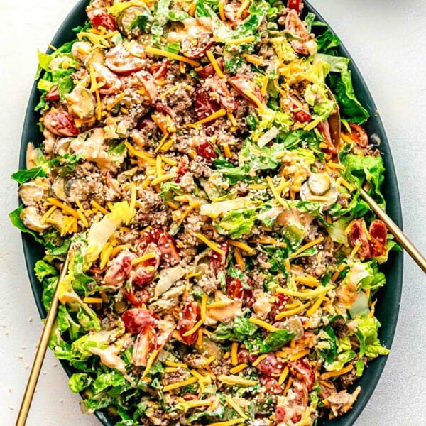 Big Mac salad tossed together on a serving platter with serving tongs.