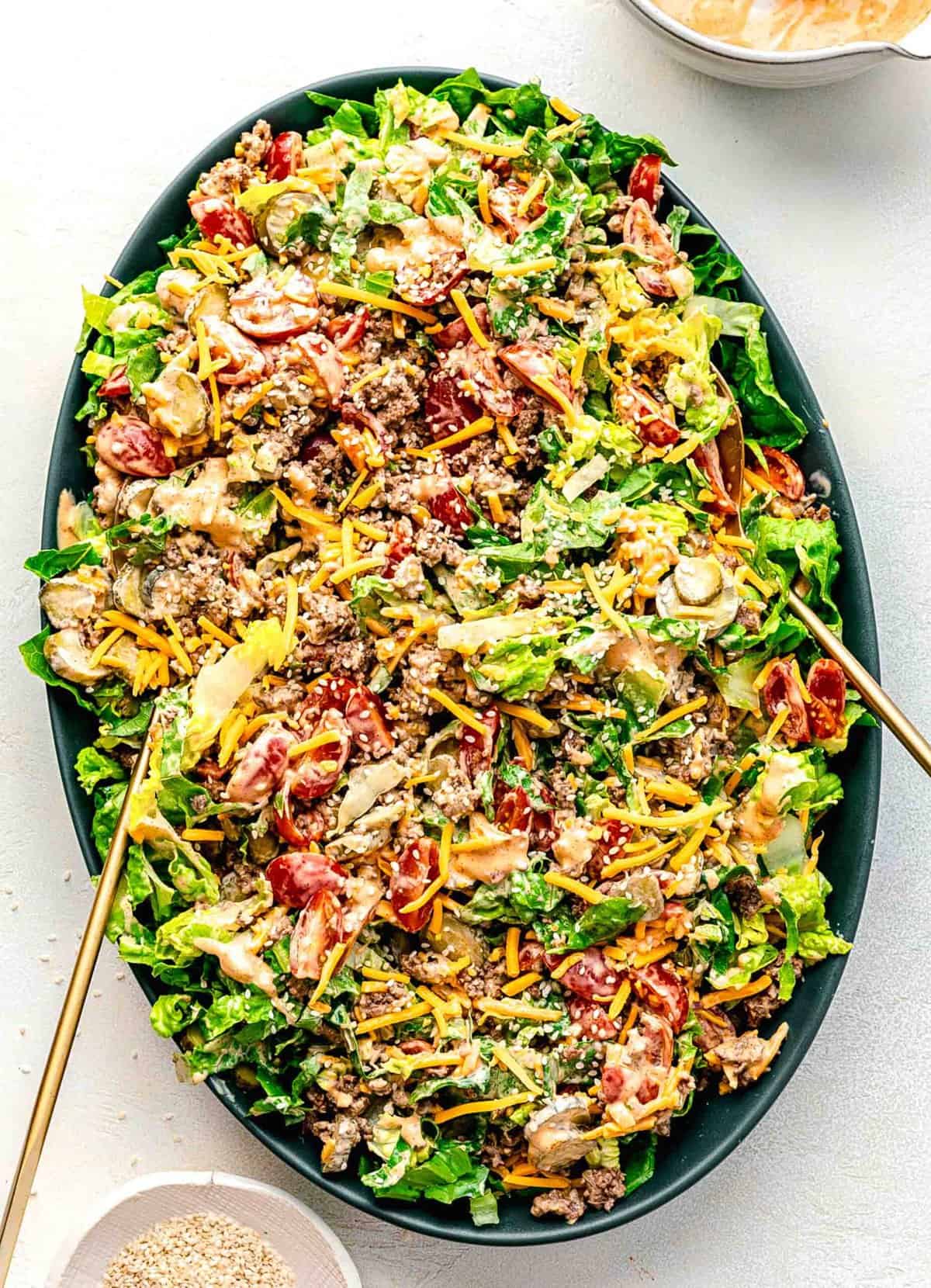 Big Mac salad tossed together on a serving platter with serving tongs.