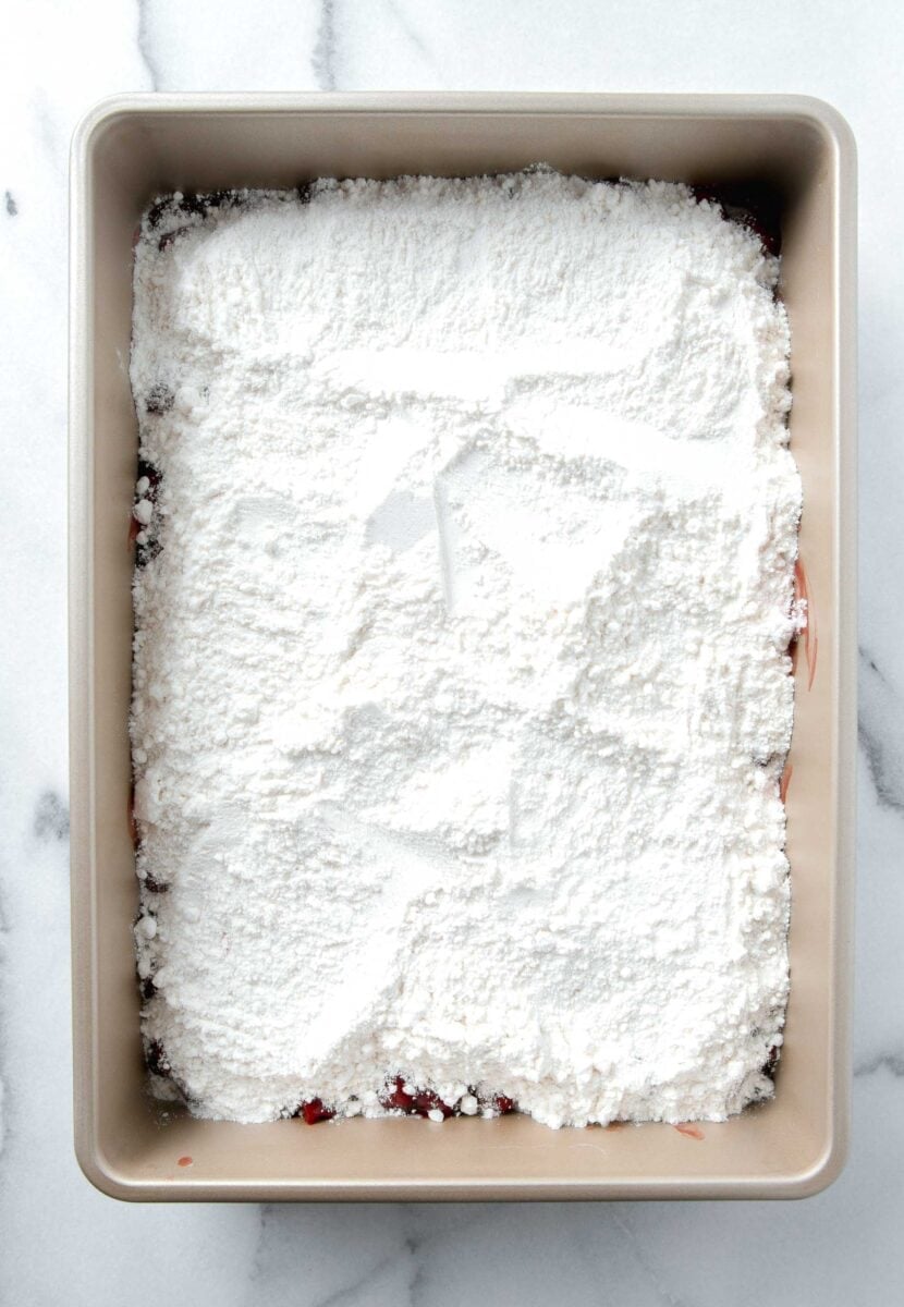 white cake mix in a 9x13 baking pan on top of the cherry pie filling