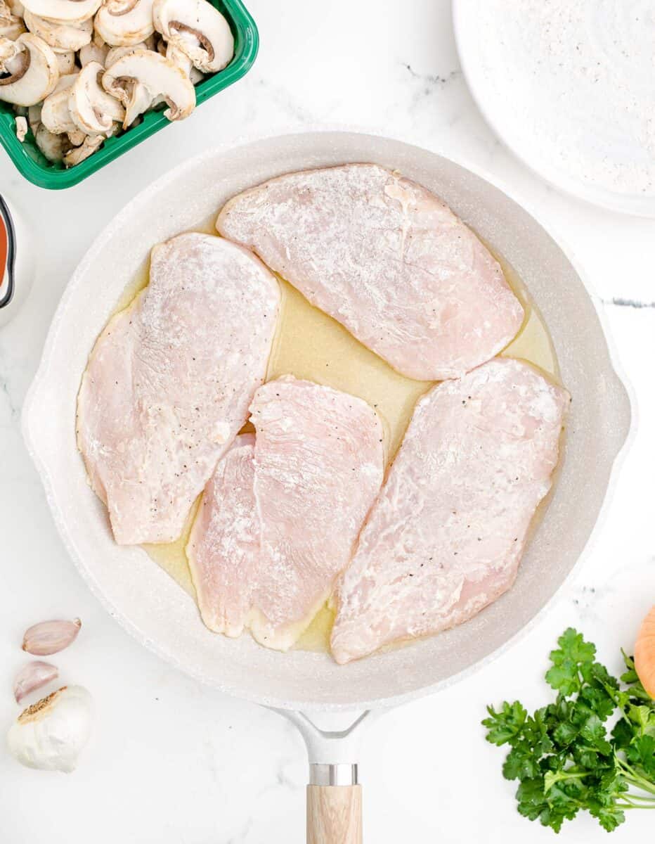 flour coated chicken breasts are in a white pot.