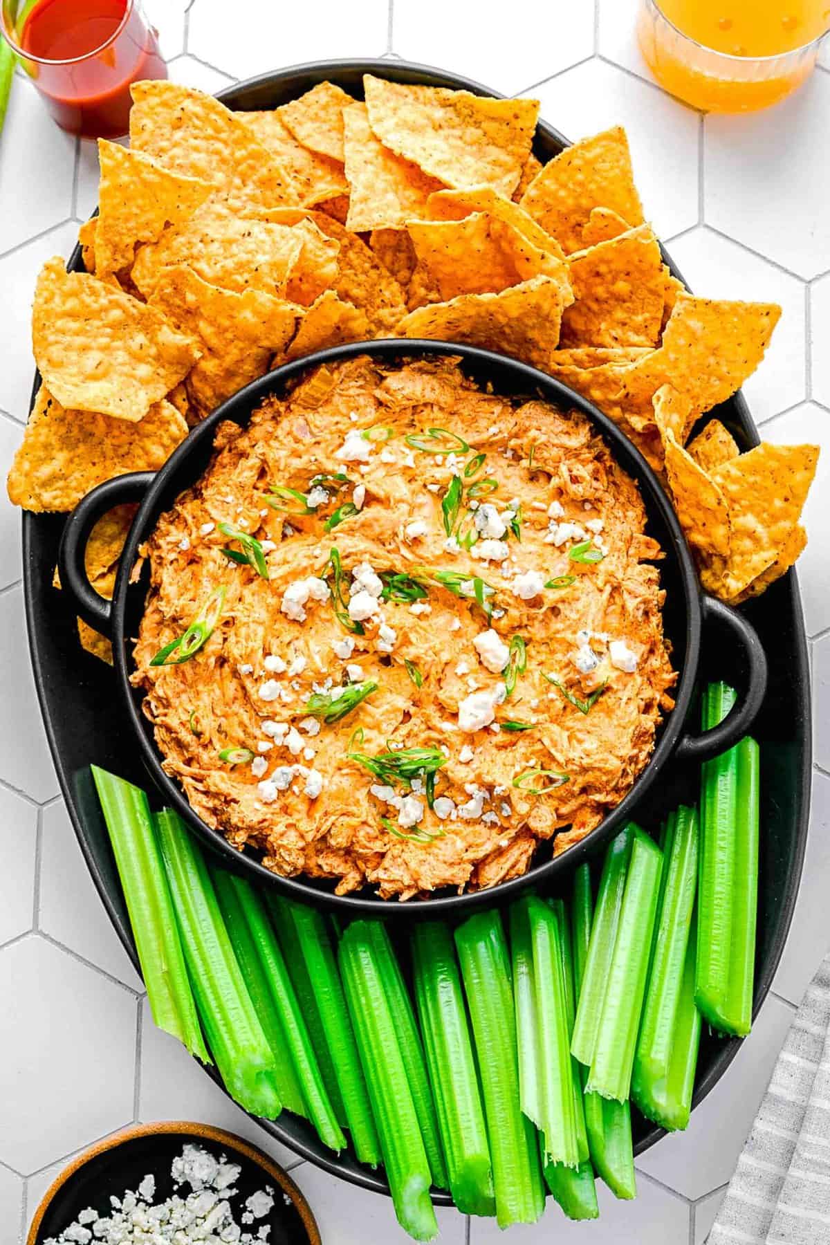 Overhead of buffalo chicken dip in a serving bowl near celery sticks and tortilla chips.