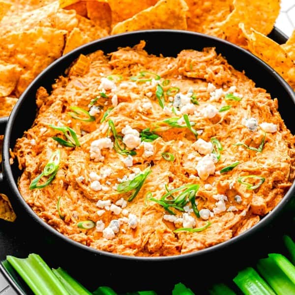 Buffalo chicken dip in a serving bowl near celery sticks and tortilla chips.