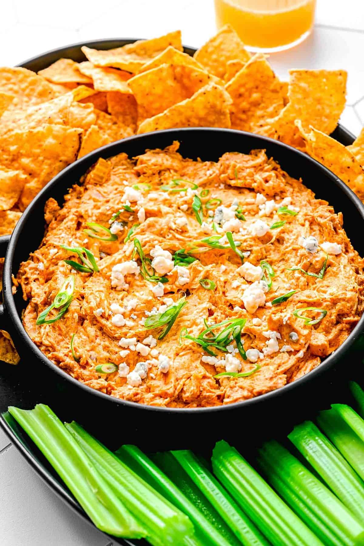 Buffalo chicken dip in a serving bowl near celery sticks and tortilla chips.