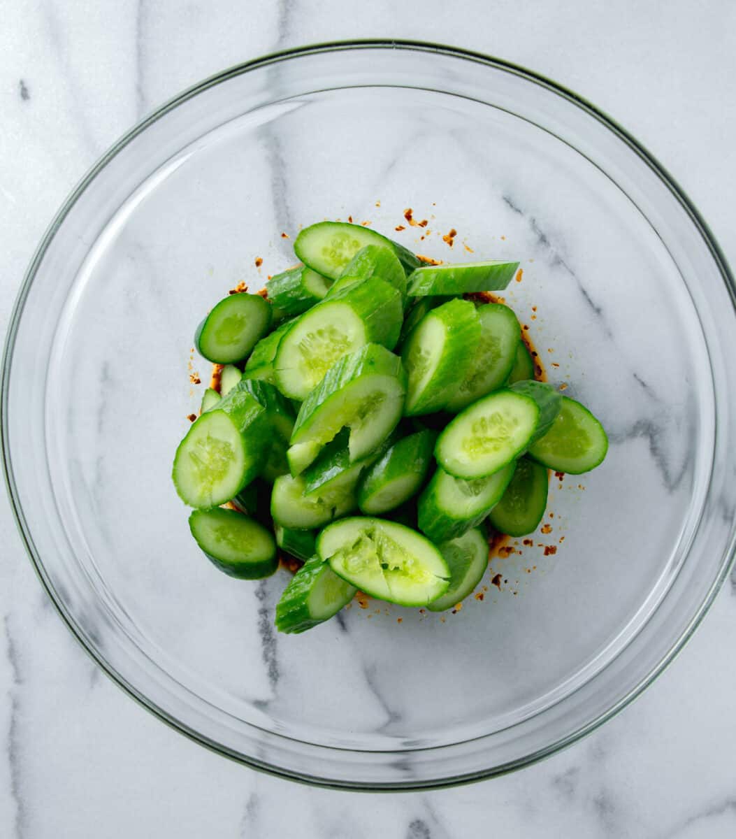 smashed cucumbers sliced at an angle in a clear bowl with sauce