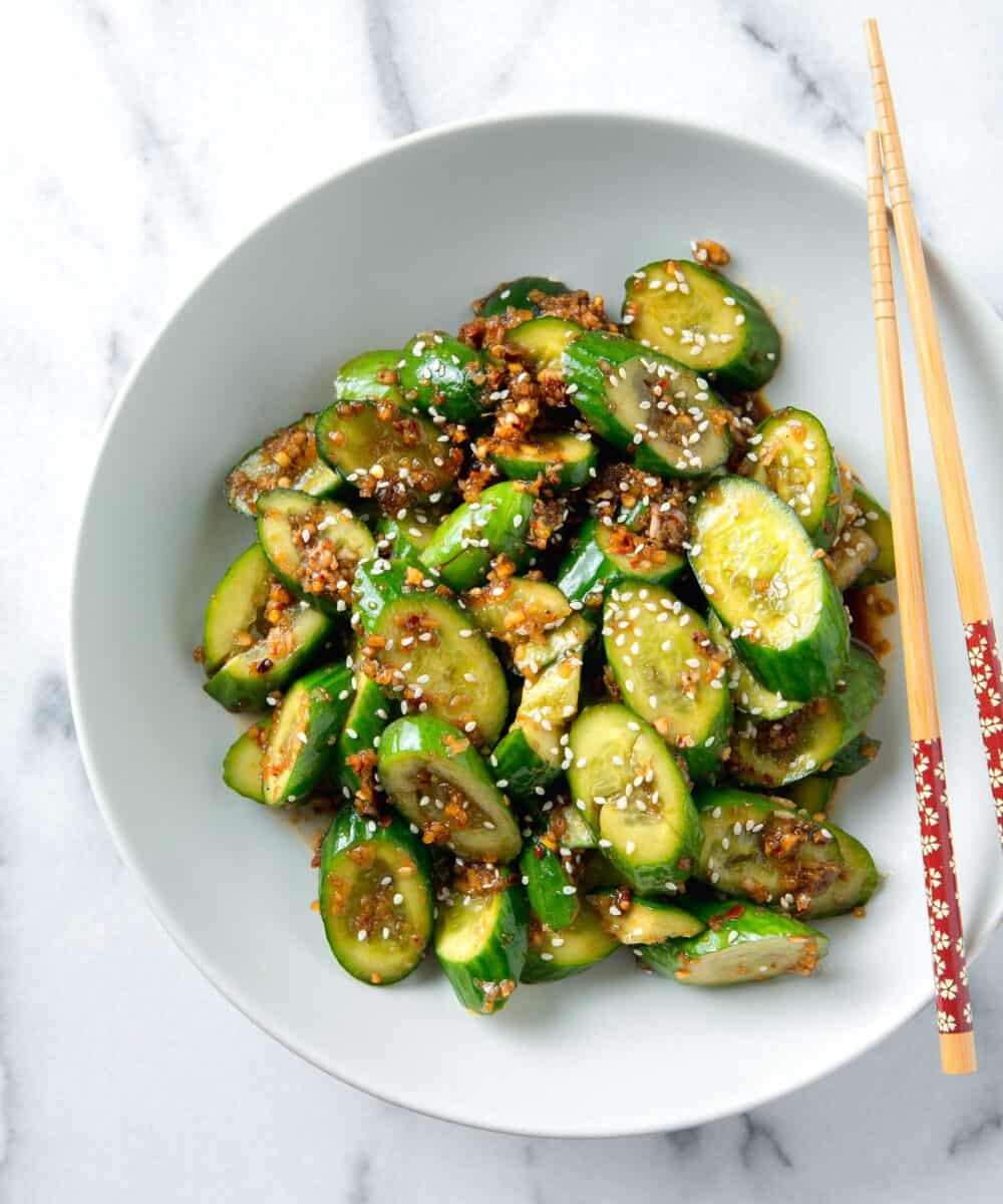 overhead image of smashed asian cucumber salad in a white bowl with wooden chopsticks next to it