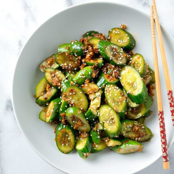 overhead image of smashed asian cucumber salad in a white bowl with wooden chopsticks next to it