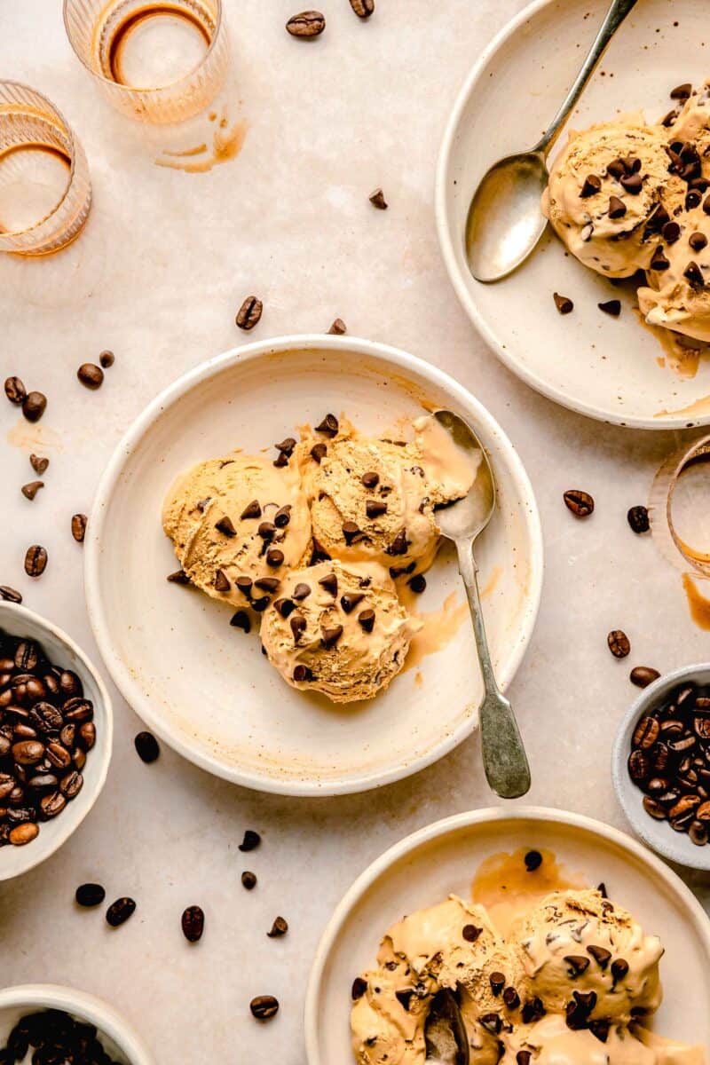 multiple scoops of espresso chocolate chip ice cream on plates with spoons and espresso beans scattered around