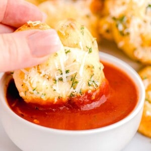 a baked garlic knot is being dipped into marinara sauce.