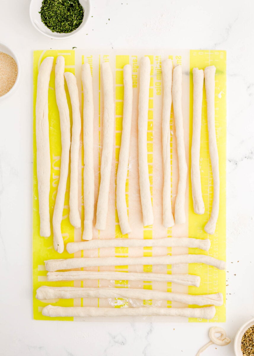 ropes of dough are placed on a yellow board.