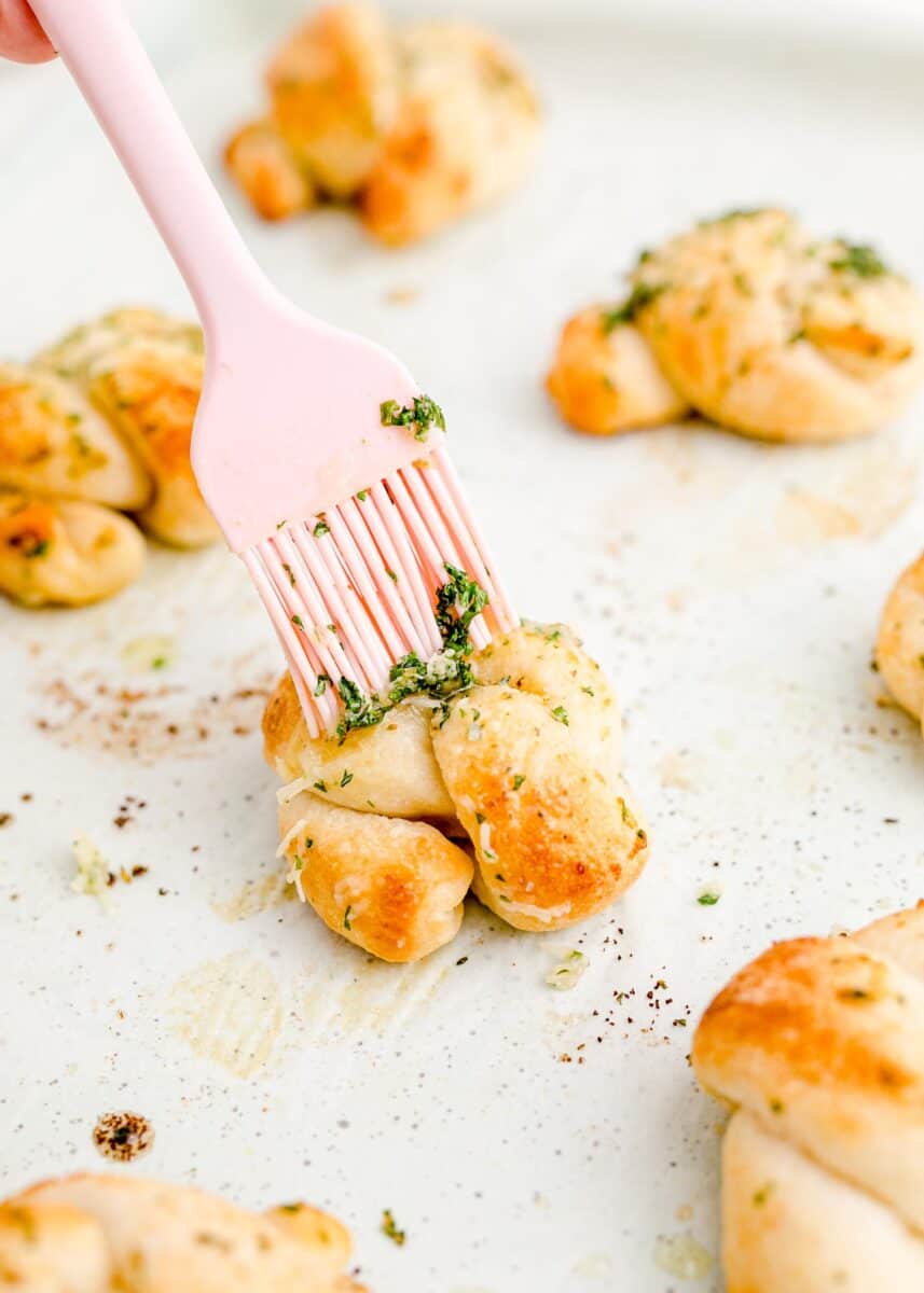 seasoned butter is being brushed onto a garlic knot.