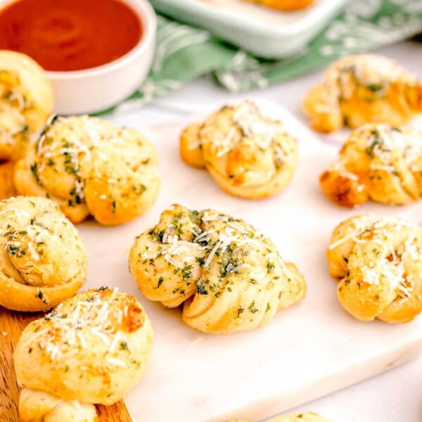 garnished, baked garlic knots are presented on a cutting board.