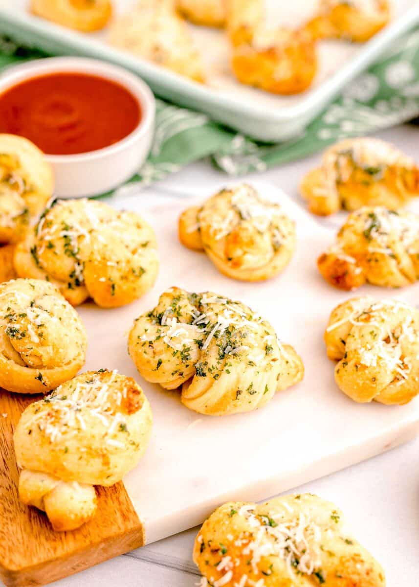 garnished, baked garlic knots are presented on a cutting board.