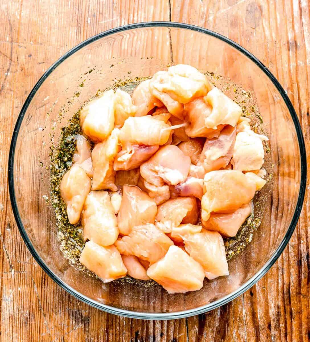 raw chicken added to the greek seasoning in the clear bowl