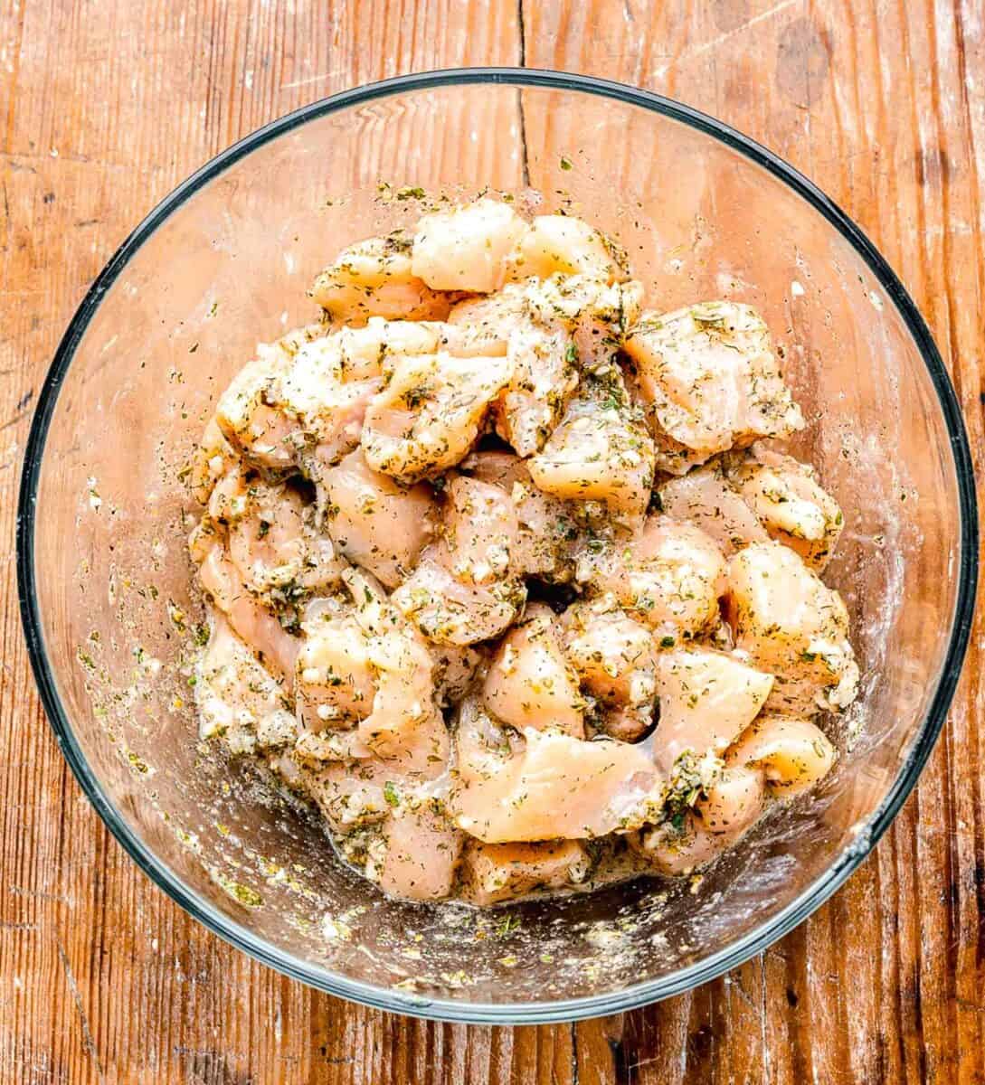 raw chicken cubes tossed in greek seasoning in a clear bowl