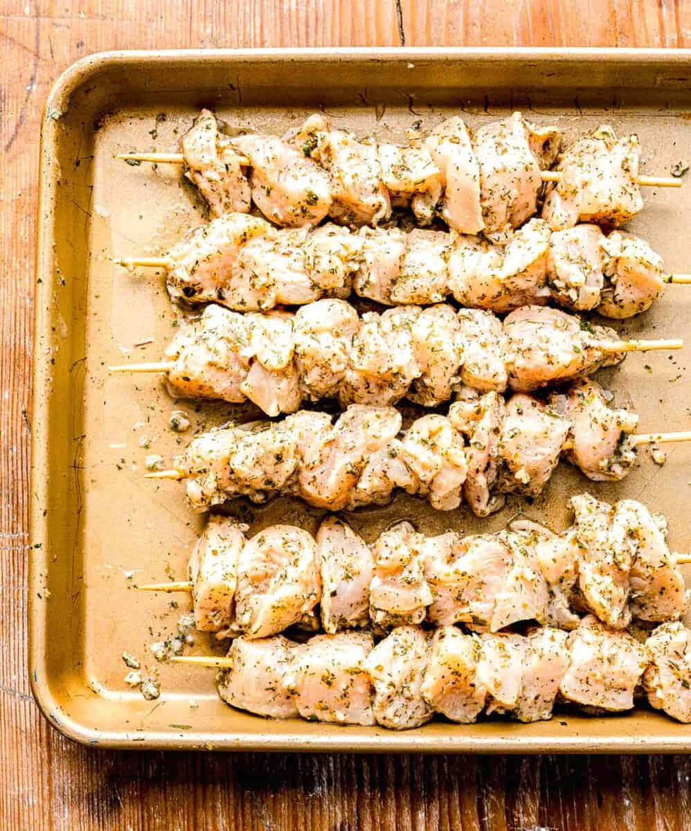 marinated chicken skewered on wooden skewers on a rimmed baking sheet