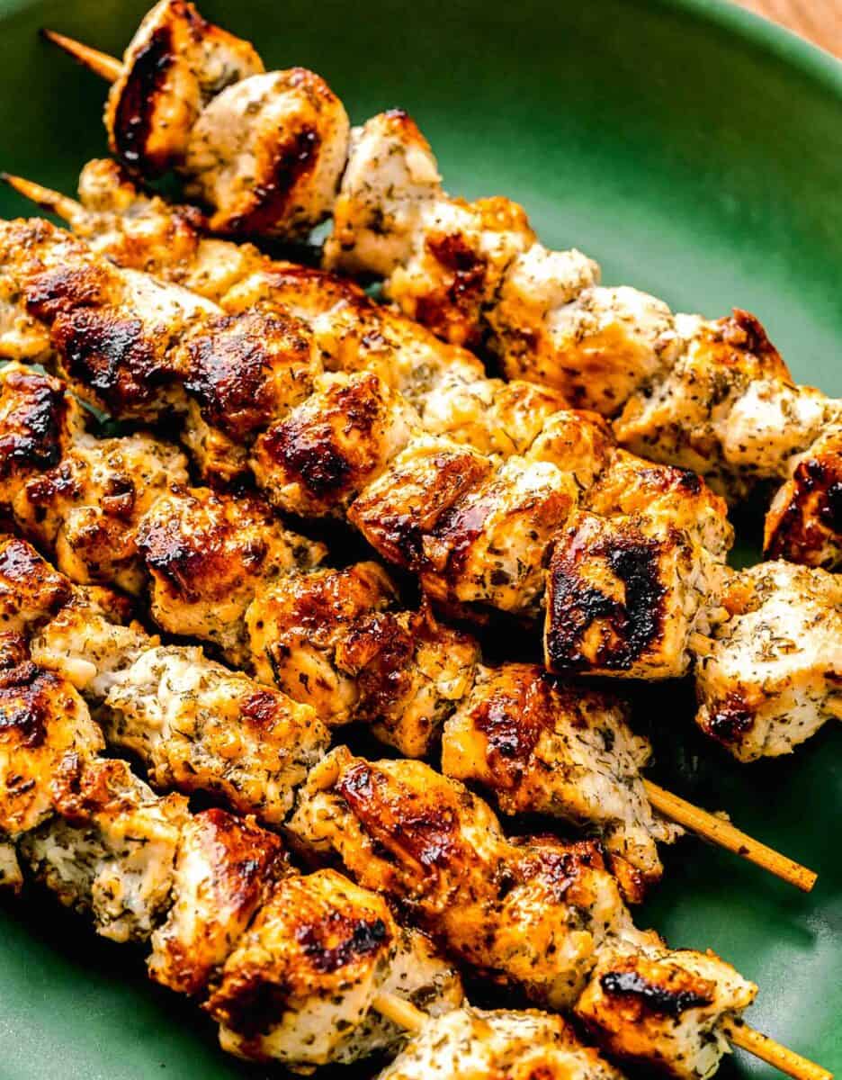 grilled greek chicken souvlaki skewers on a green platter