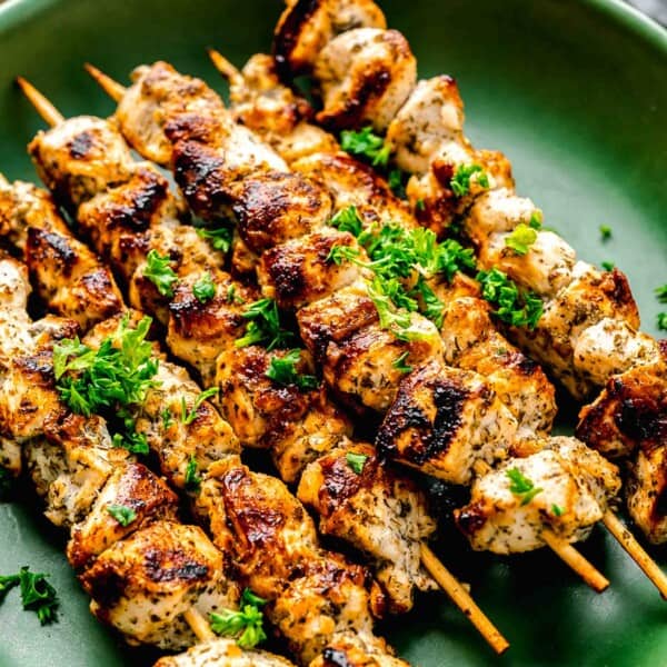 greek chicken souvlaki skewers on a green plate with fresh parsley on top