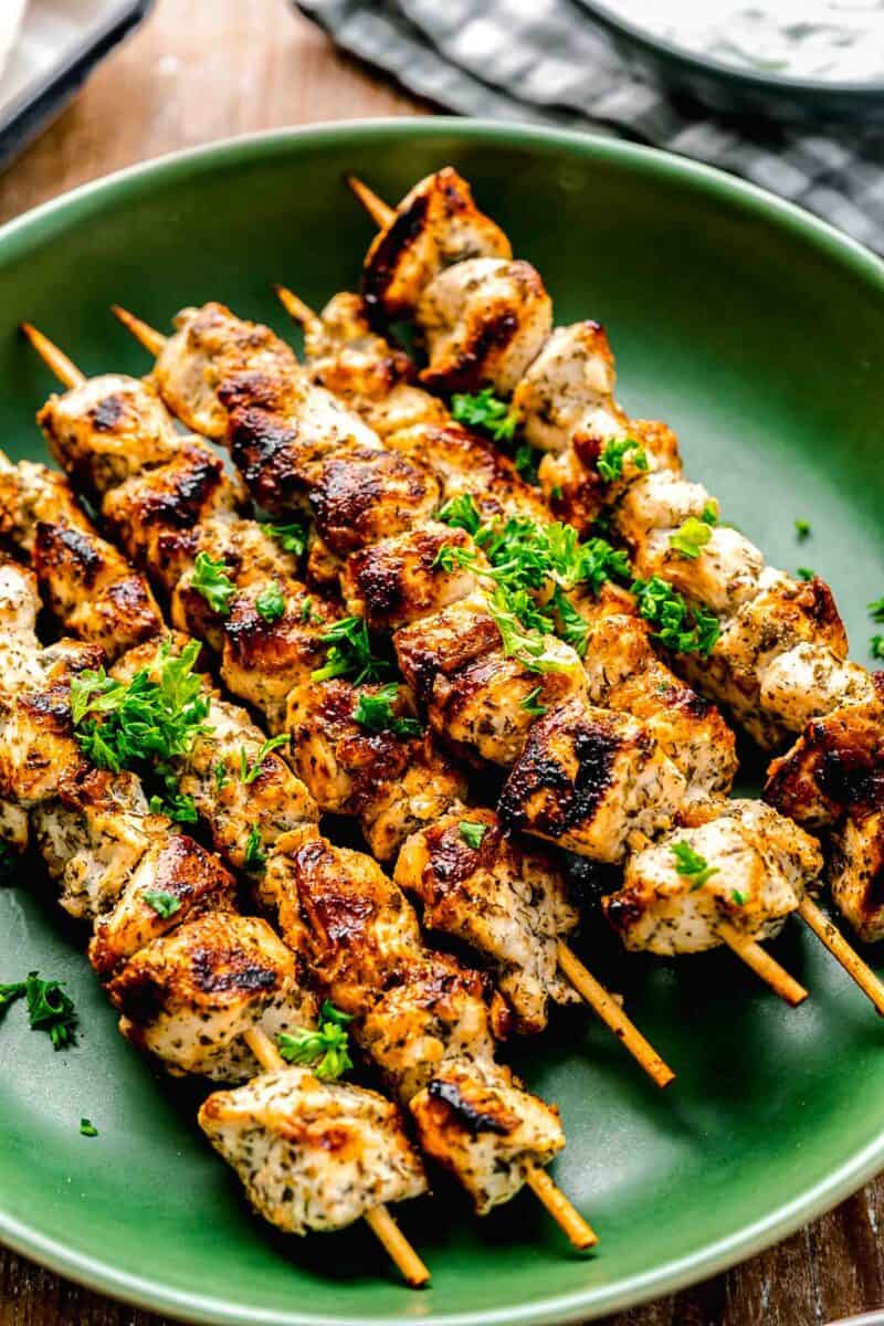 greek chicken souvlaki skewers on a green plate with fresh parsley on top