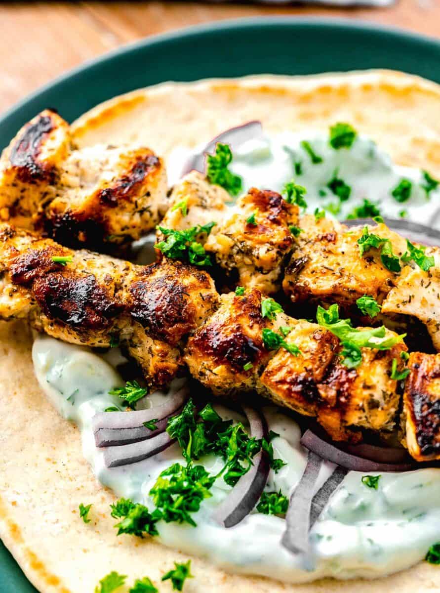 greek chicken souvlaki skewers on top of pita and tzatziki sauce