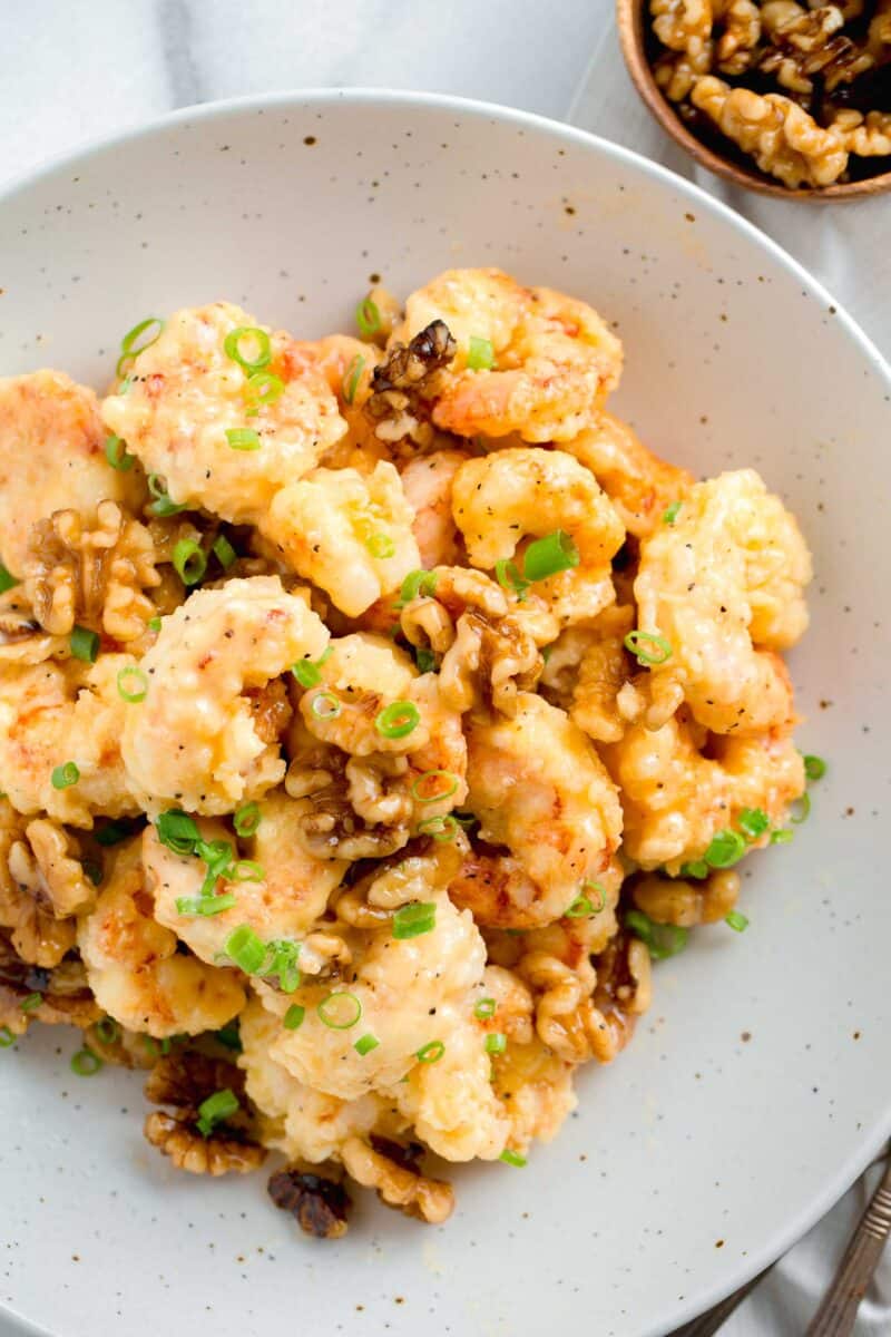 honey walnut shrimp in a speckled bowl next to a wooden bowl of walnuts