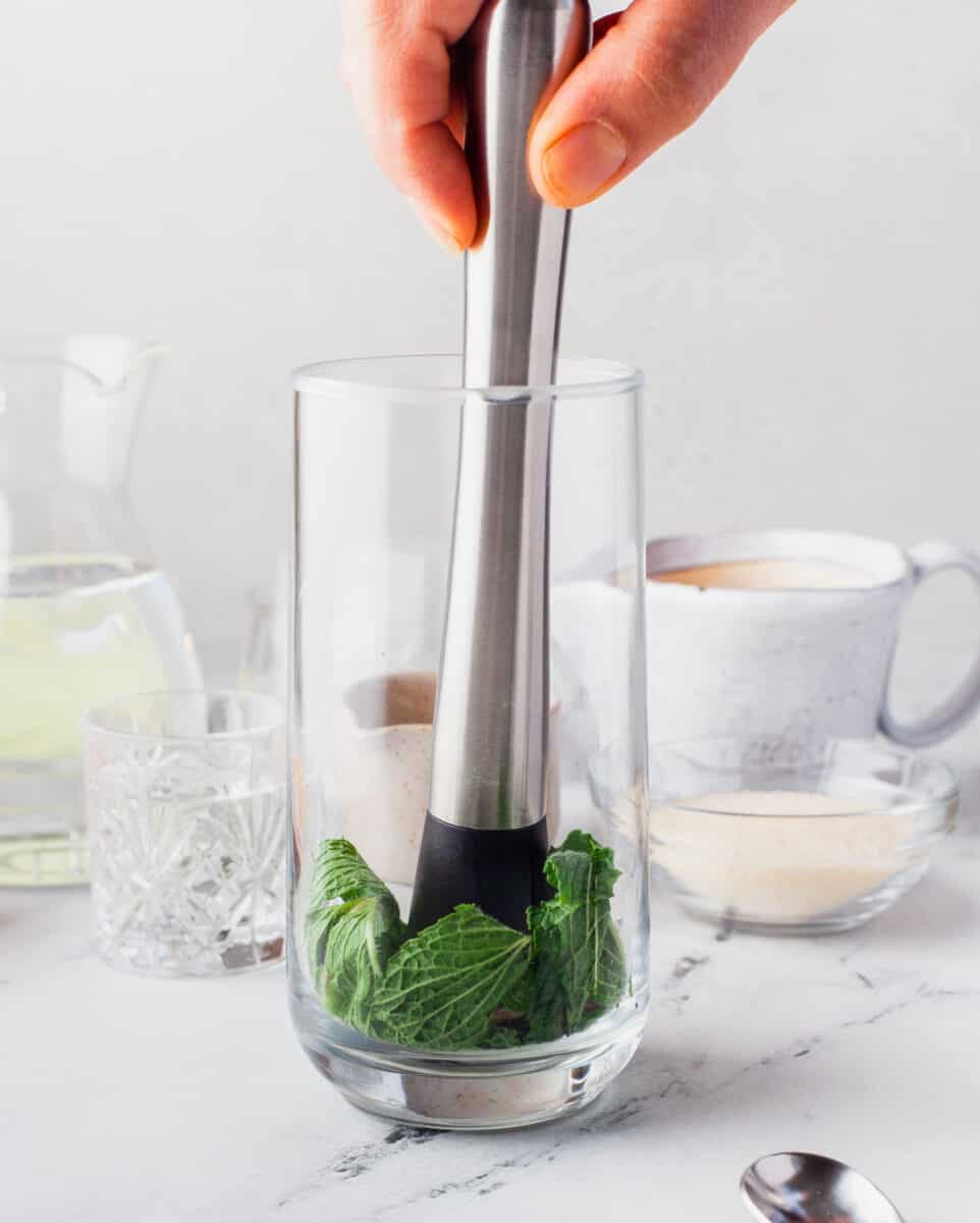 mint leaves are being muddled in the bottom of a glass