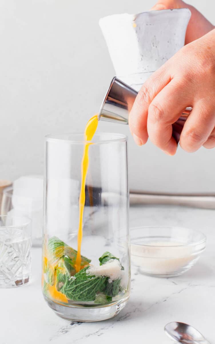 orange juice is being poured into a glass with mint leaves