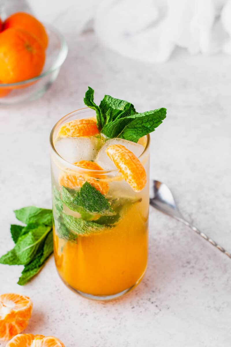 a cocktail spoon is placed next to a garnished glass of orange mojito