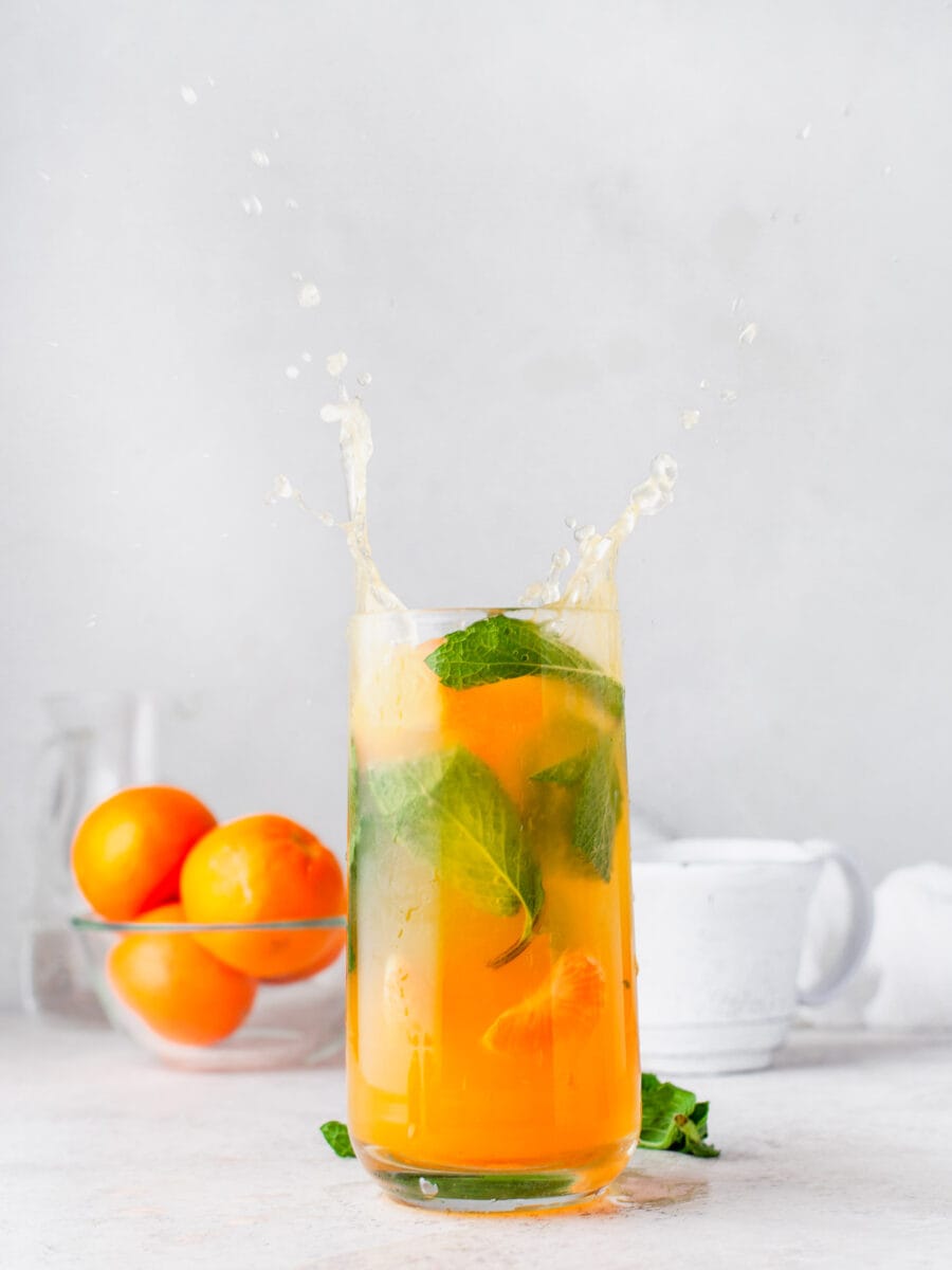 an orange mojito is splashing in a tall glass