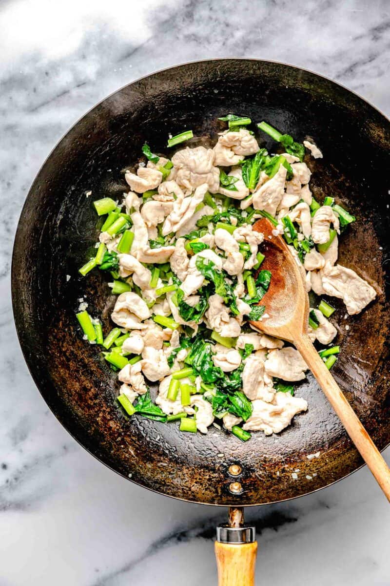 chicken and gai lan being cooked in a wok with a wooden spoon