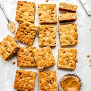a dozen cookie bars are placed next to a small bowl of peanut butter.