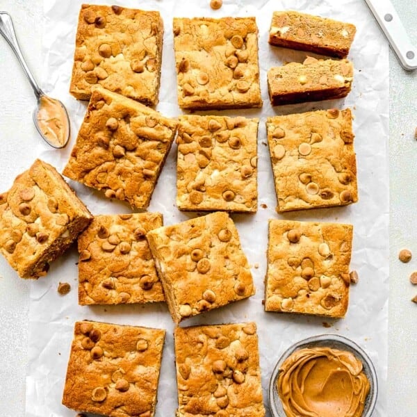 a dozen cookie bars are placed next to a small bowl of peanut butter.