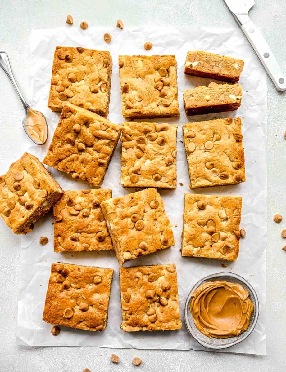 a dozen cookie bars are placed next to a small bowl of peanut butter.