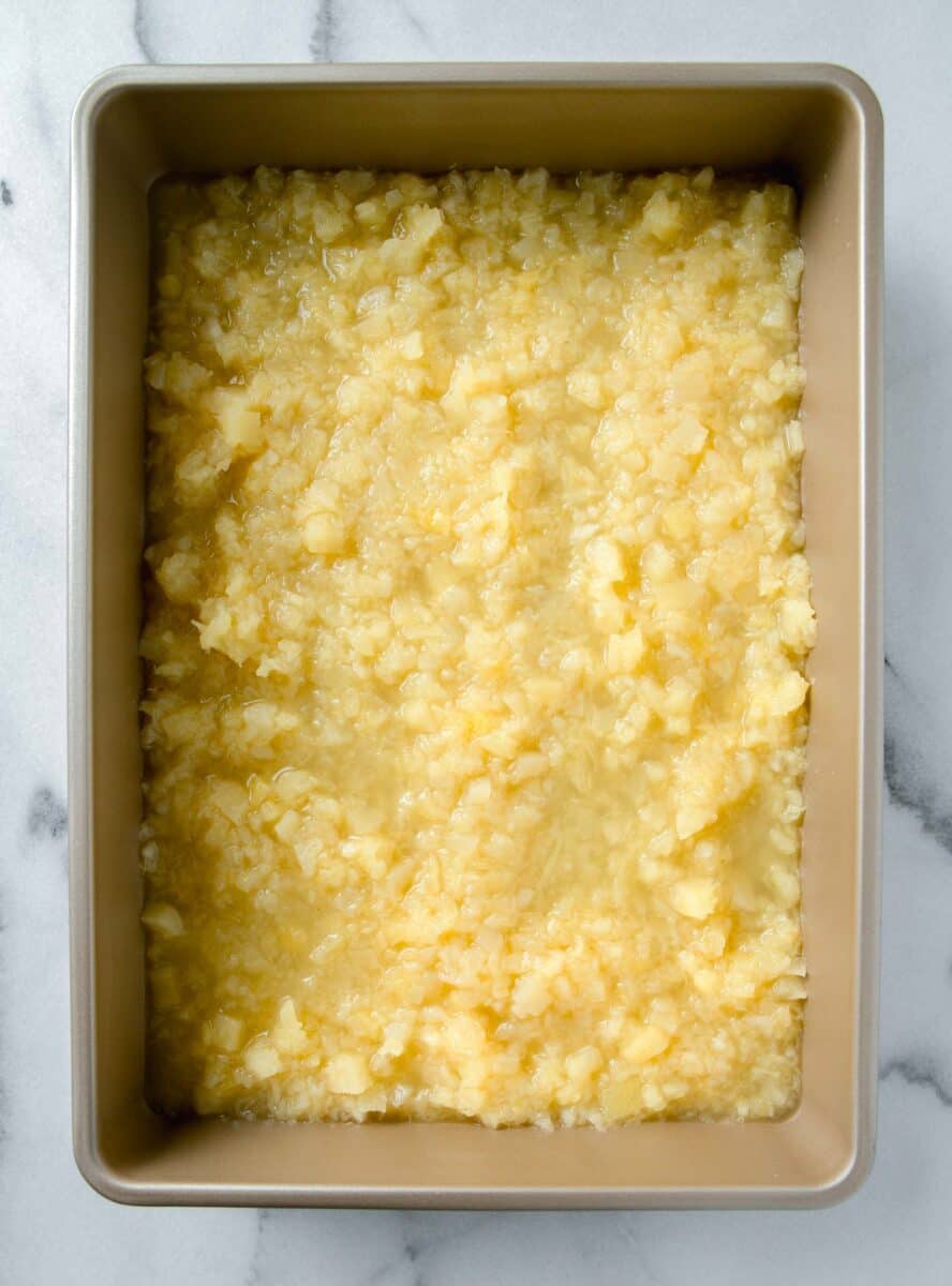 crushed pineapple in an even layer in a 9x13 gold baking dish