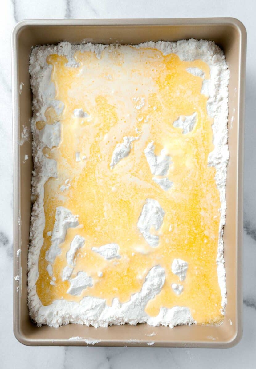 melted butter added on top of white cake mix in an even layer in a 9x13 gold baking dish
