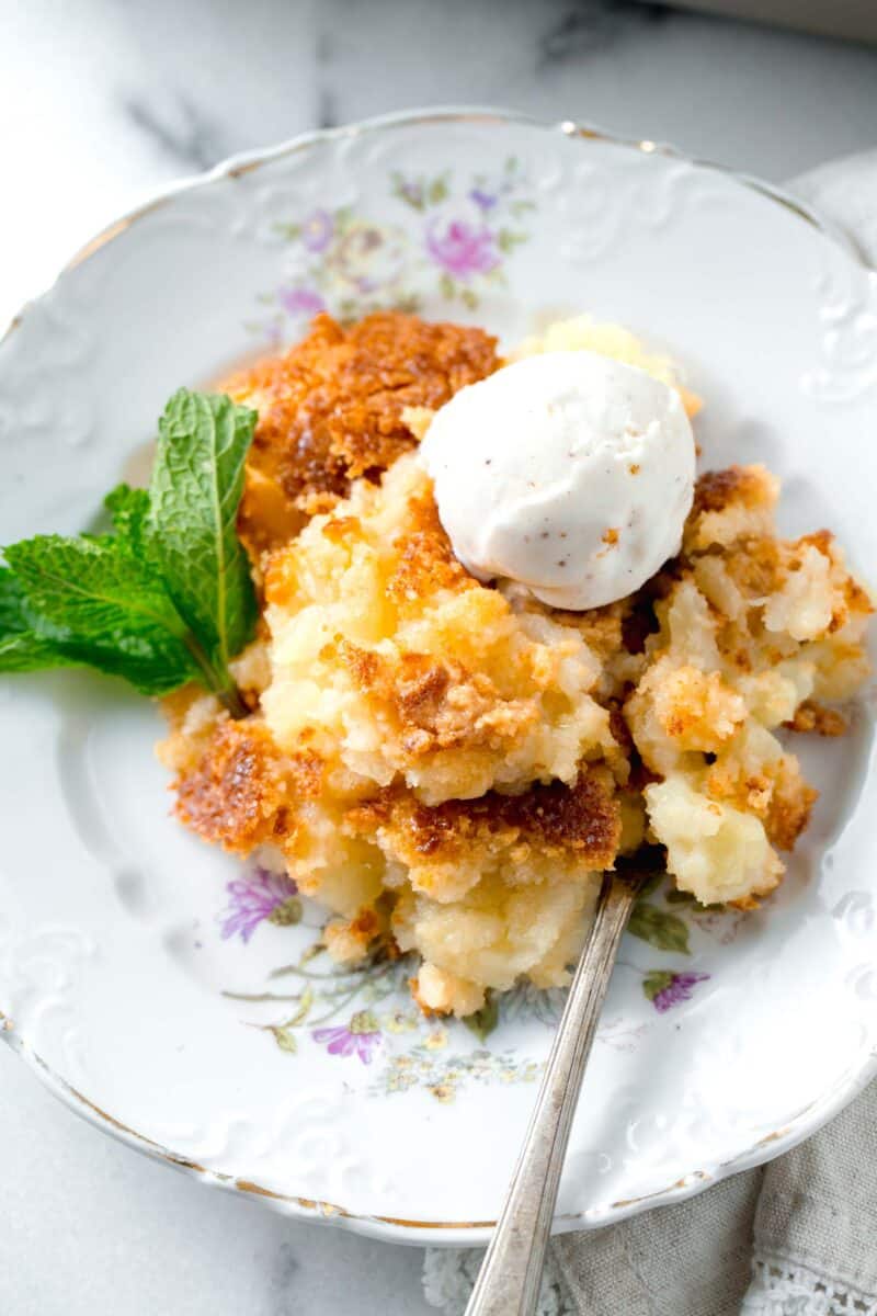 pineapple dump cake on a floral gold-lined dessert plate next to a sprig of fresh mint with an ice cream scoop on top