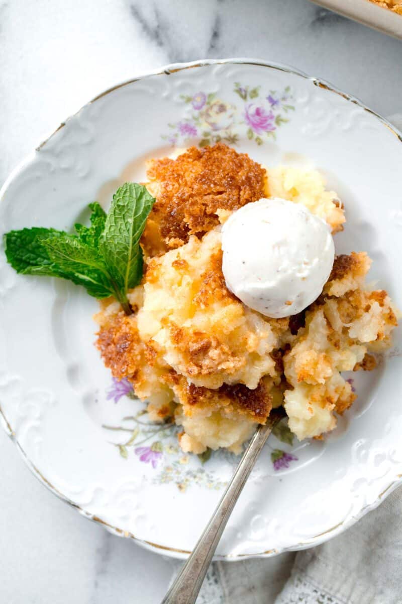 pineapple dump cake on a floral gold-lined dessert plate next to a sprig of fresh mint with an ice cream scoop on top