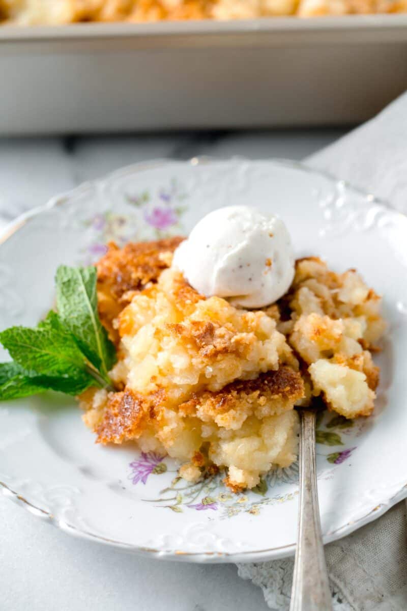 pineapple dump cake on a floral gold-lined dessert plate with a spoon next to a sprig of fresh mint with an ice cream scoop on top